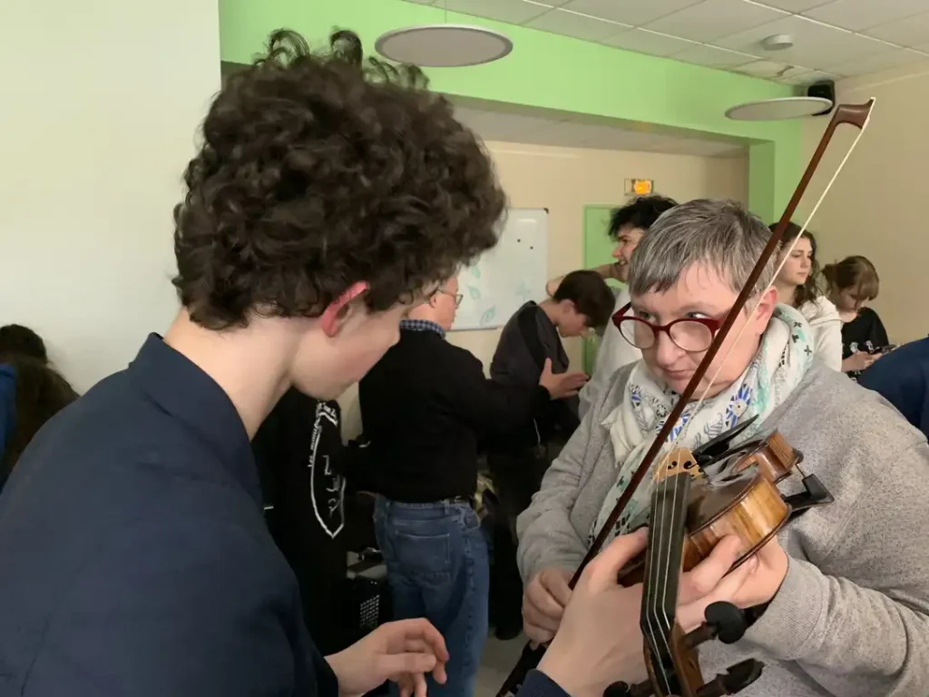 Un lycéen tend un violon à une résidente du foyer.