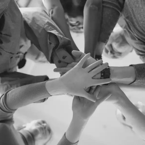 Une photo en noir et blanc où des mains se rassemble autour d'un cercle d'humain.